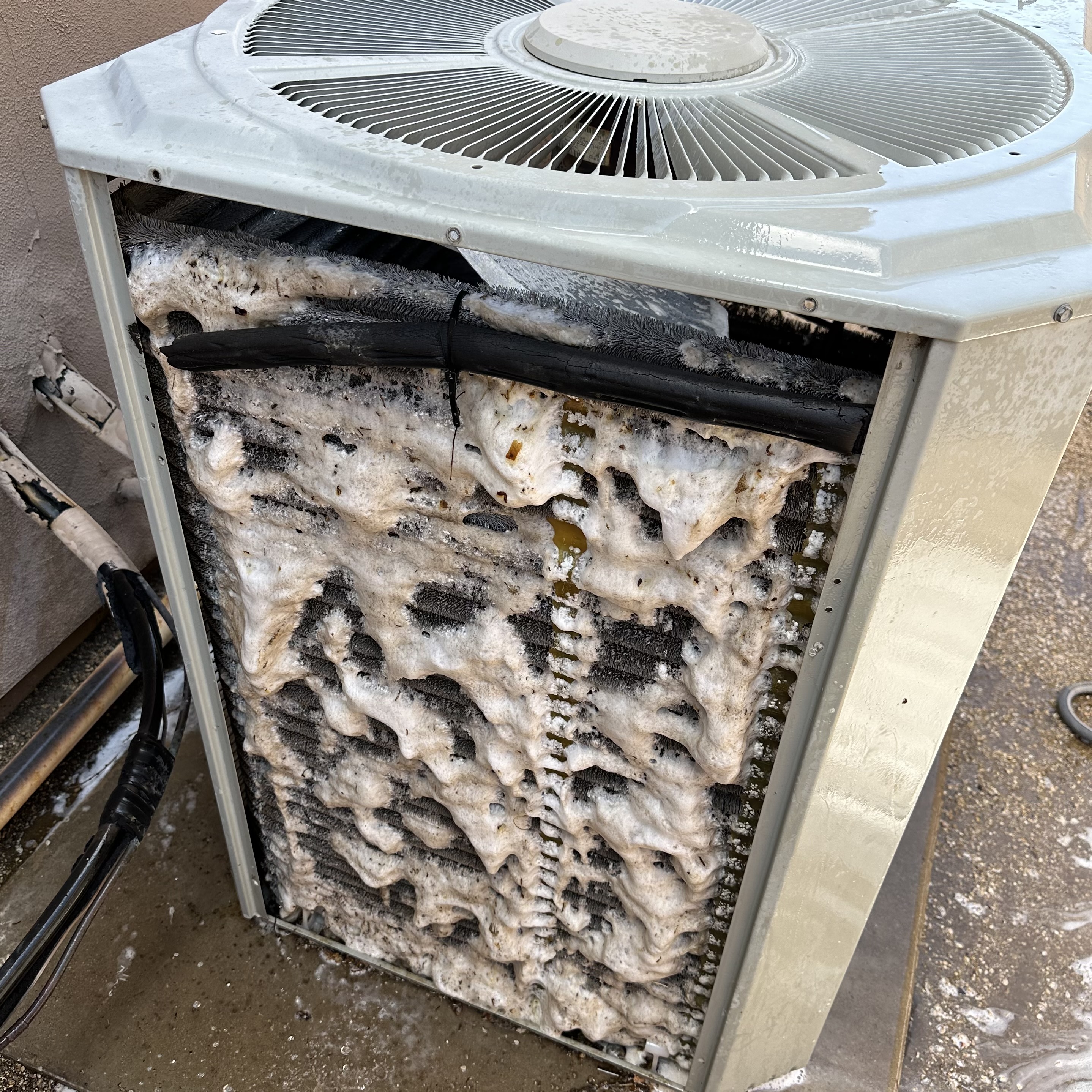 A dirty HVAC condenser coil covered in foaming cleaner.